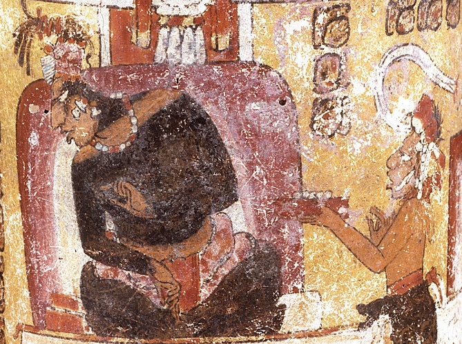 Regla sentada con las piernas cruzadas y la espalda descansando sobre un cojín grande como asistente le ofrece un platillo pequeño, Vaso Pintado (Enthroned Maya Lord and Asistdants), c. 650-750 C.E., Maya, jarrón cilíndrico, cerámica, 16.51 x 20.32 cm (Dumbarton Oaks Museum)