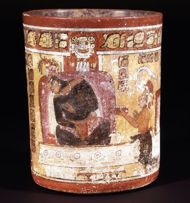 Ruler sitting with legs crossed and back resting on a large cushion as an attendant offers him a small dish, <em>Painted Vessel (Enthroned Maya Lord and Attendants)</em>, c. 650-750 C.E., Maya, cylinder vase, ceramic, 16.51 x 20.32 cm (Dumbarton Oaks Research Library and Collection, Washington, D.C.)
