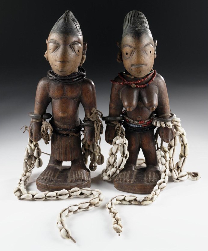 Ibeji, Yoruba, Nigeria, carved wood with attached personal ornaments including glass bead necklaces and girdles, metal armlets and strings of cowries attached from the wrists (National Museum of Scotland)