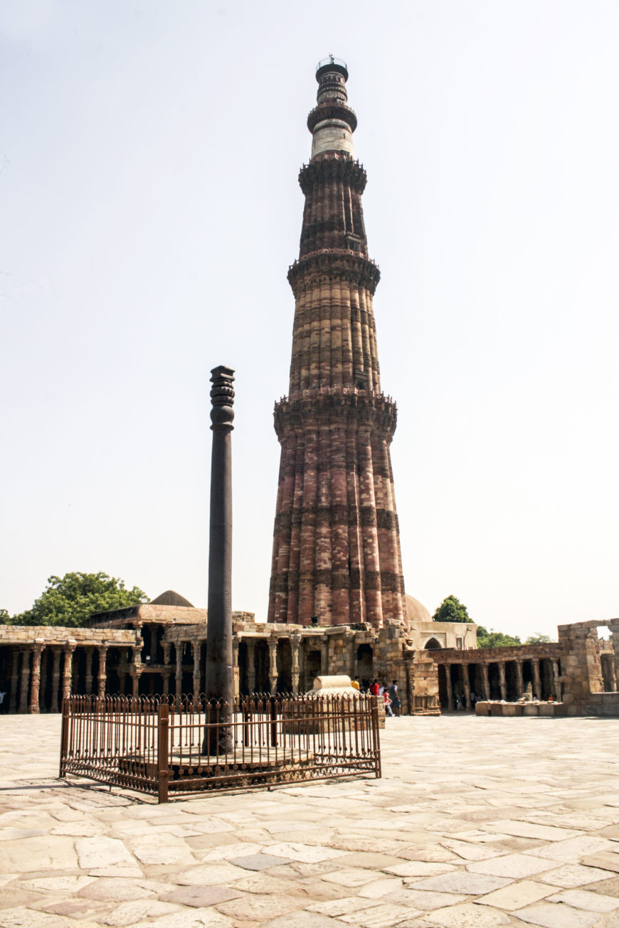 El Qutb Minar de 238 pies de altura al fondo, c. 1192, complejo arqueológico Qutb, Delhi (foto: Indrajit Das, CC BY-SA 4.0). En primer plano se encuentra un pilar de hierro del siglo IV al V y la mezquita Qutb del siglo XII.