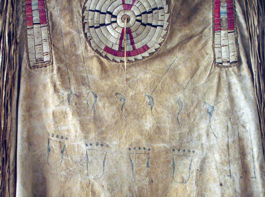 Detail of faces, coup sticks, and bear claws, quilled war shirt (back), c. 1800-1820. Native tanned hide, porcupine quills, red trade cloth, dyes, and sinew. 34 x 43 in. (Denver Art Museum)