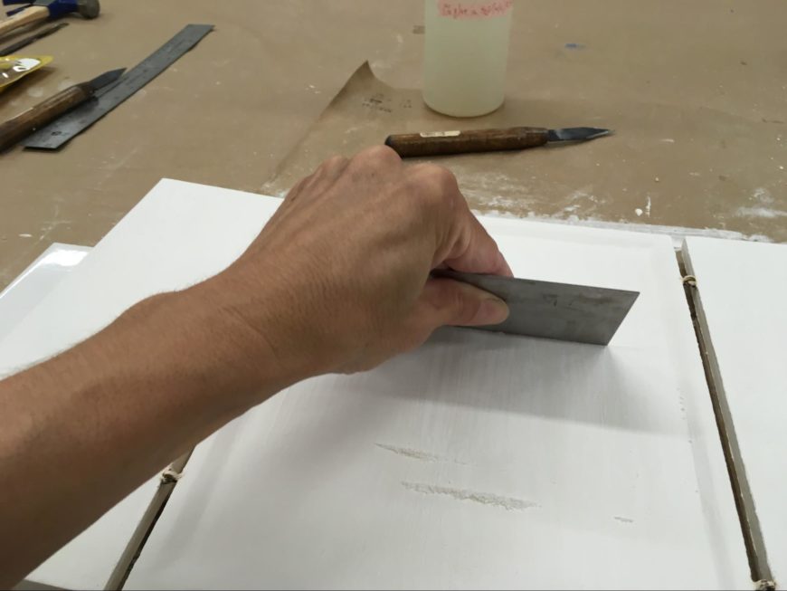 Smoothing the dried gesso on the central panel with a cabinet scraper