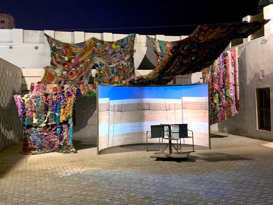 Figure 2 Suchitra Mattai, Imperfect Isometry, 2019; videos of border walls (Jerusalem/Palestine, US/Mexico) and prison wall, vintage sari tapestry, chalk drawing, spinning found Kalba merry-go-round; Sharjah Biennial 14 (2019)