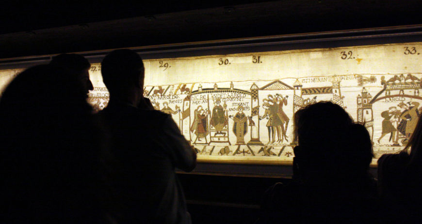 Viewing the Bayeux tapestry at the Bayeux Tapestry Museum; Bayeux tapestry, c. 1070, embroidered wool on linen, 20 inches high (Bayeux Museum) (photo: boris does burg, CC BY-NC-SA 2.0)