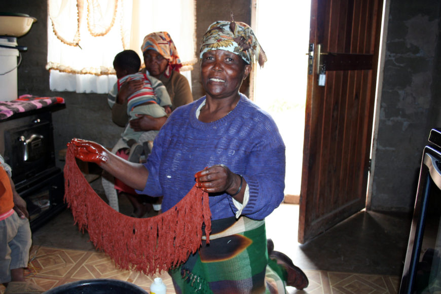 Artist Maria Mofokeng holding the fringe of a thethana which has been freshly dyed with letsoku, 2008. Photo by David M. M. Riep