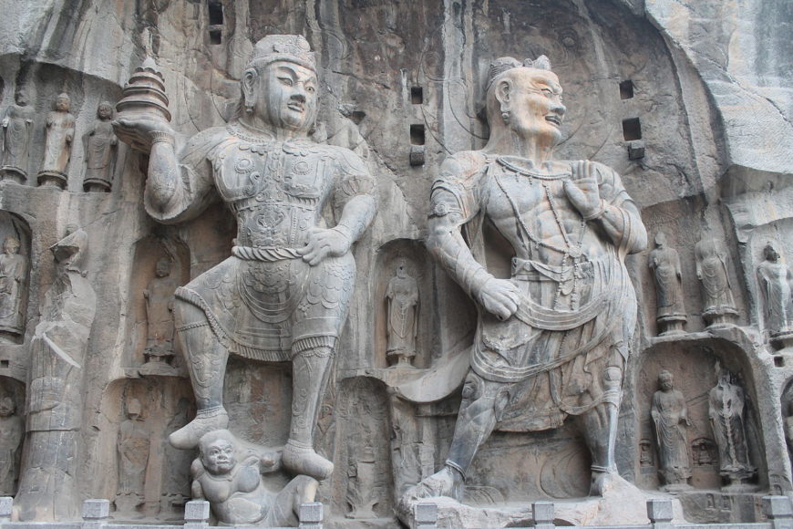 Vaiśravana, one of The Four Heavenly Kings, is on the left (indicated by the stupa in his right hand). Vajrapāṇi (on the right) are spiritual beings that wield the thunderbolt, 673–75 C.E., Tang dynasty, limestone, Luoyang, Henan province (photo: Dominik Tefert, public domain)