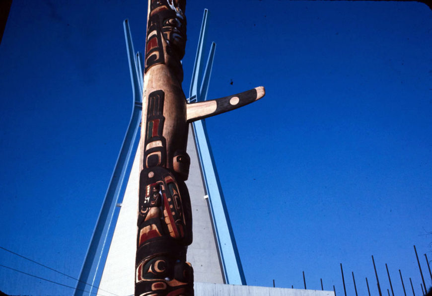 Detail of totem pole by Henry and Tony Hunt and tipi in the background at the Indians of Canada Pavilion, with Harry Hunt performing the Raven Dance in the foreground. 1967 (Library and Archives Canada / Canadian Corporation for the 1967 World Exhibition)
