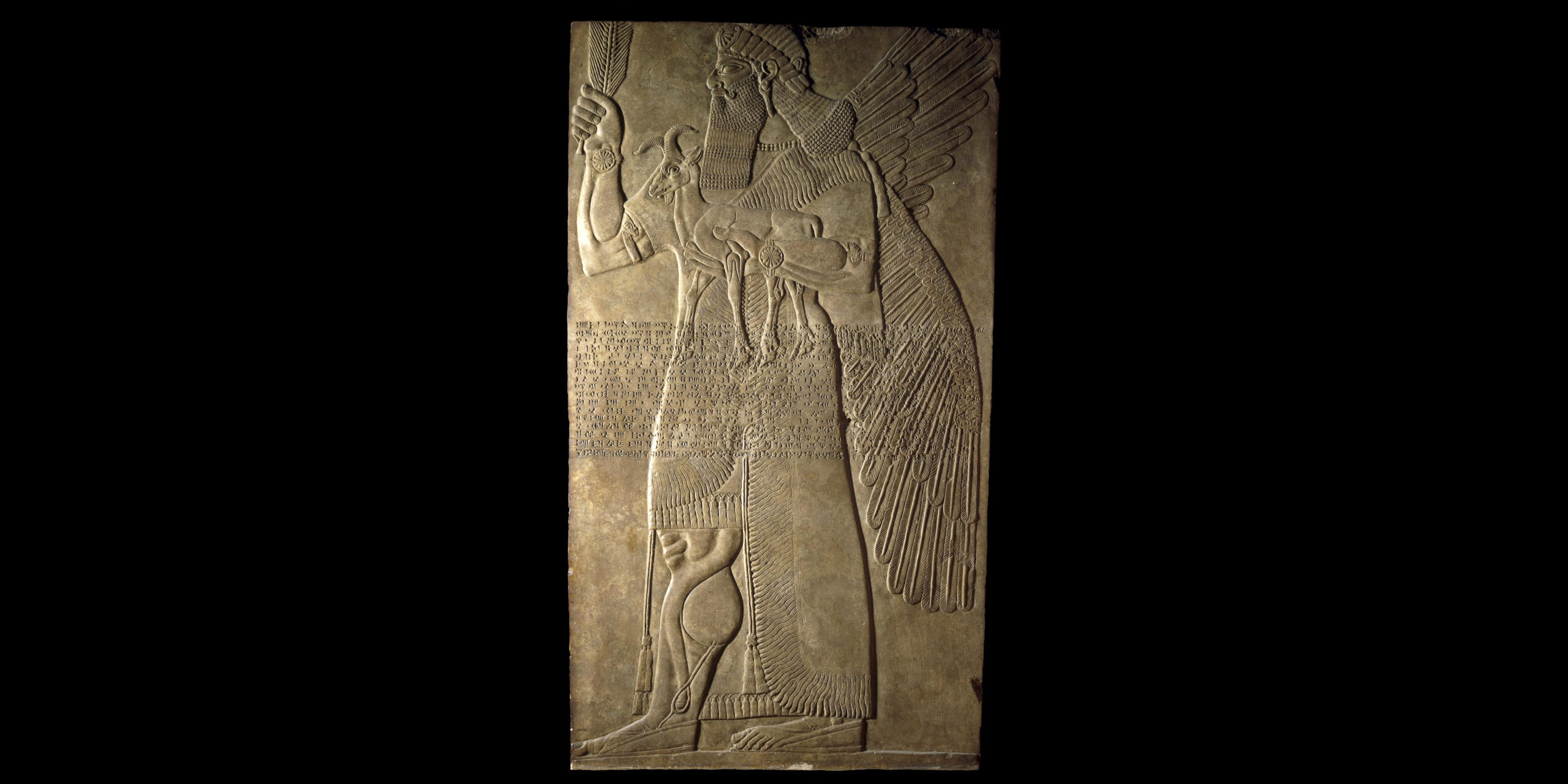 Protective Spirit Relief from the North-West Palace of Ashurnasirpal II, 883-859 B.C.E., Neo-Assyrian, alabaster, 224 x 127 x 12 cm (extant), Nimrud (ancient Kalhu), northern Iraq © Trustees of the British Museum. One of a pair which guarded an entrance into the private apartments of Ashurnasirpal II. The figure of a man with wings may be the supernatural creature called an apkallu in cuneiform texts. He wears a tasselled kilt and a fringed and embroidered robe. His curled moustache, long hair and beard are typical of figures of this date. Across the body runs Ashurnasirpal's "Standard Inscription," which records some of the king's titles.