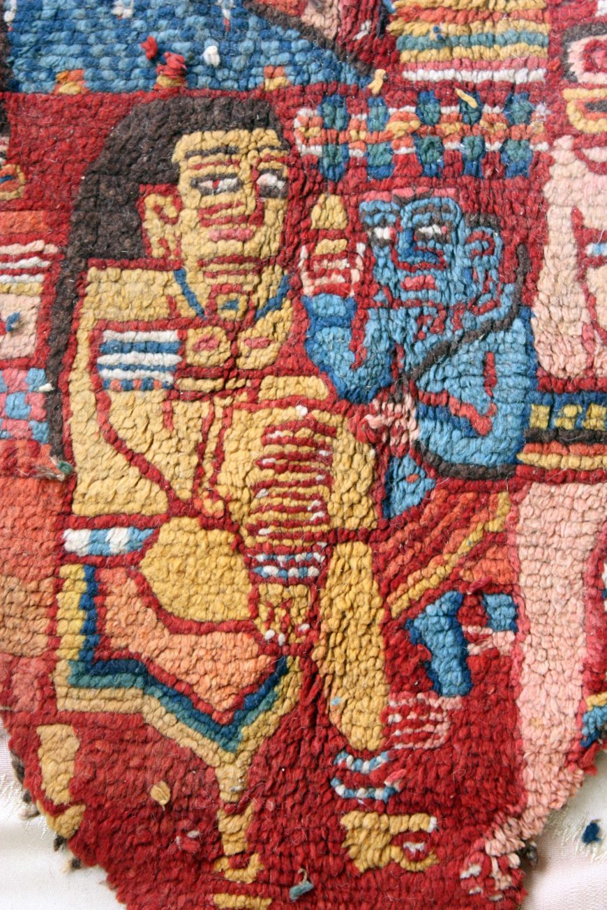 Detail with two figures, possibly showing Yashoda sitting in Indian royal posture lalitāsana, and the little blue Krishna holding a butter ball motif in the right hand. Knotted Carpet with human figures and Brahmi/Khotanese inscriptions, 5th–6th century C.E., Shanpula Township, Khotan District, Xinjiang Uygur Autonomous Region, China (photo: He Zhang)