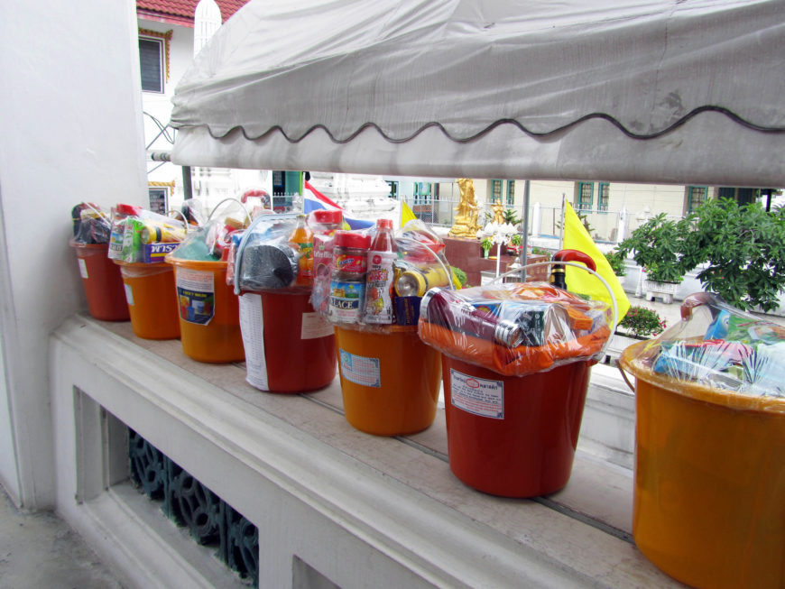 Gift buckets on a ledge at Wat Mahanpharam, Bangkok, containing a variety of useful items donated to the monks by layfolk. Visible are various food products, sandals, flashlights, and umbrellas (photo by the author).