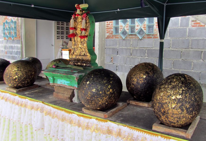Luk nimit on display at Wat Kaew Fa Chulamanee, Bangkok, next to a bai sema stone, during the renovation and reconsecration of the ordination hall. Temple visitors paying respect to the stones have pressed gold leaf onto their surfaces as a devotional act (photo: Jessica Patterson, CC BY-NC-SA)