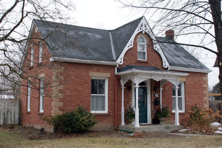 A red brick house with yellow brick details. The house has an added front porch framing the entrance.