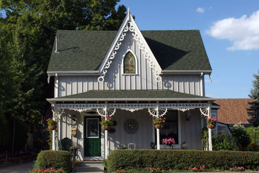 A wooden house painted gray with a green roof. The porch and gable are embellished with wooden trim.