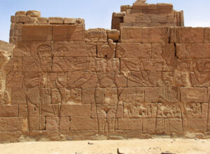 Queen Amanitore (left) and King Natakamani (right) flanking the three-headed, four-armed rendering of Apedemak (center) from the back of the Lion Temple or back of the Pylon?, Naga, Sudan. (Photo: Stuart Tyson Smith, CC BY-SA 4.0)