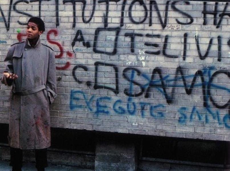 Jean-Michel Basquiat posing next to SAMO graffiti