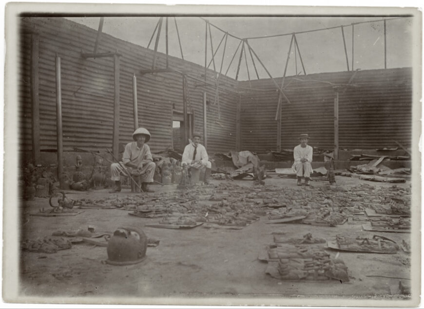 Reginald Kerr Granville, Interior of King's compound burnt during fire in the siege of Benin City, with three British officers of the Punitive Expedition [from left, Captain C.H.P. Carter 42nd, F.P. Hill, unknown], seated with bronzes laid out in foreground, 1897, photograph, 16.5 x 11.5 cm (Pitt Rivers Museum, Oxford University)