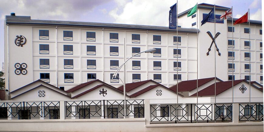 The old City Hotel was renovated and reopened as Golden Tulip Hotel in Kumasi, Ghana. The photograph shows the front view of the left wing of the building. On the building’s façade are adinkra symbols, such as Gye Nyame in the upper left corner. The adinkra symbol, akofena, is to the right of the photograph underneath a sign that says the name of the hotel (which is obscured by the flags). Consisting of two swords that cross to form an “X” shape, akofena refers to power and authority. Golden Tulip Hotel, 2008 (photo: ZSM, CC BY-SA 3.0)