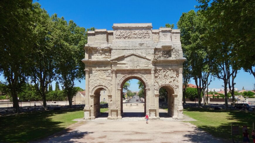 View of the south side of the Arch at Orange, facing town, with the road out of town visible through the archway. Modern traffic is diverted around the arch. Arch at Orange, France, 20s B.C.E. stone, 19.21 x 19.57 x 8.4 m (photo: Jean-Louis Zimmermann, CC BY-SA 2.0)