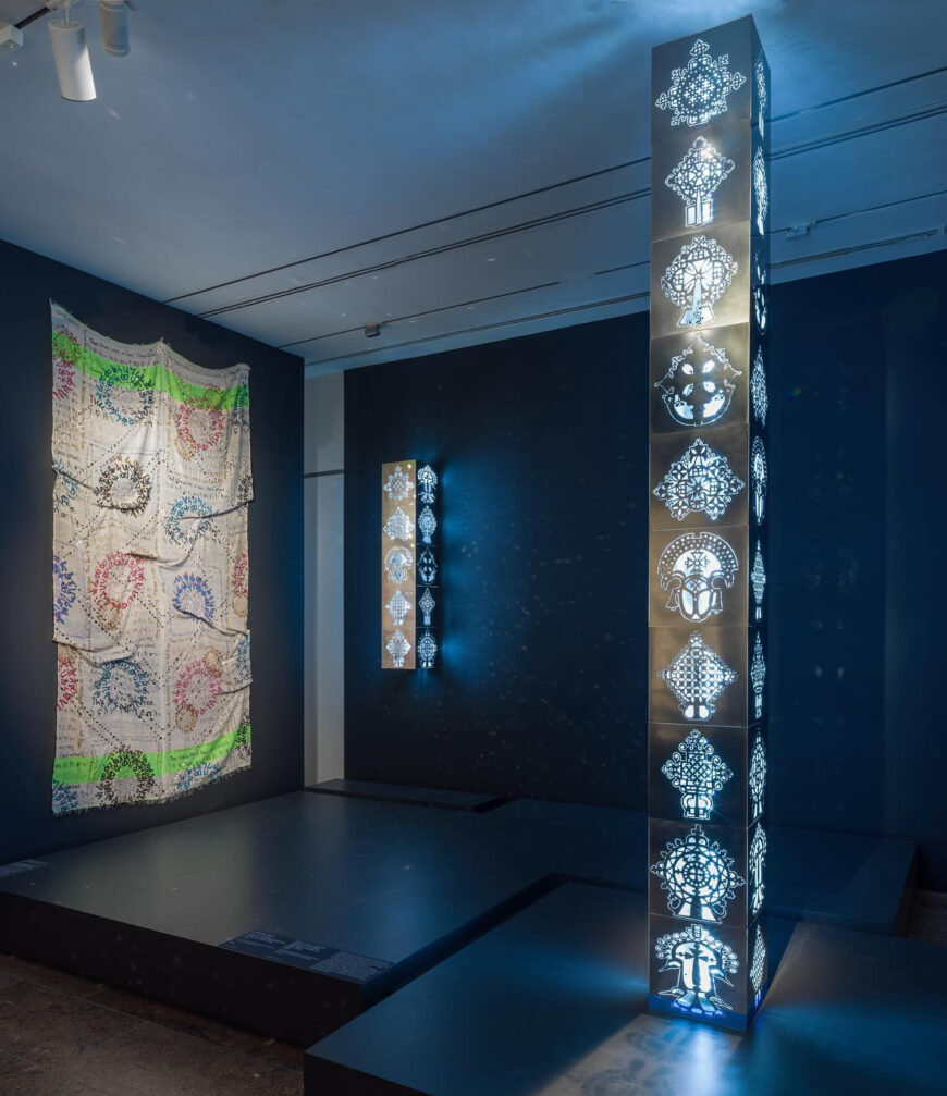 Tsedaye Makonnen, Nefsé Nets’a Mawt’at Däbtäras ነፍስን : ነፃ : ማውጣት :: ደብተራ :: The Soul Is Set Free Magic Scrolls I–V, 2023, cotton, water-based screenprinting ink, and mirror acrylic; and Tsedaye Makonnen, Tsehai | ጠሐይ | Sunlight, 2023, mirrored stainless steel, plexiglass, LED tubes, wall-mounted cleats with corresponding hardware, 152.4 x 30.5 x 30.5 cm (Collection of the artist; photo: Anna-Marie Kellen) © Tsedaye Makonnen