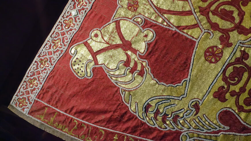 Camel (detail), Mantle of Roger II, 1133/34 (Norman Sicily, Italy), textiles, patterned samite (kermes dye), gold and silk embroidery, pearls, gold with cellular enamel, rubies, spinels, sapphires, garnets, glass, tablet weave, 146 x 345 cm (Kunsthistorisches Museum, Vienna, XIII 14; photo: Steven Zucker, CC BY-NC-SA 2.0)