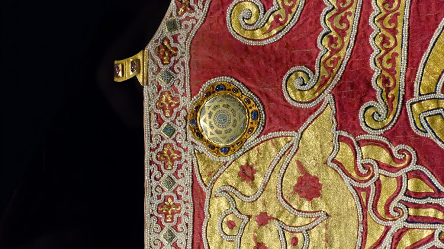 Clasp and medallion (detail), Mantle of Roger II, 1133/34 (Norman Sicily, Italy), textiles, patterned samite (kermes dye), gold and silk embroidery, pearls, gold with cellular enamel, rubies, spinels, sapphires, garnets, glass, tablet weave, 146 x 345 cm (Kunsthistorisches Museum, Vienna, XIII 14; photo: Steven Zucker, CC BY-NC-SA 2.0)